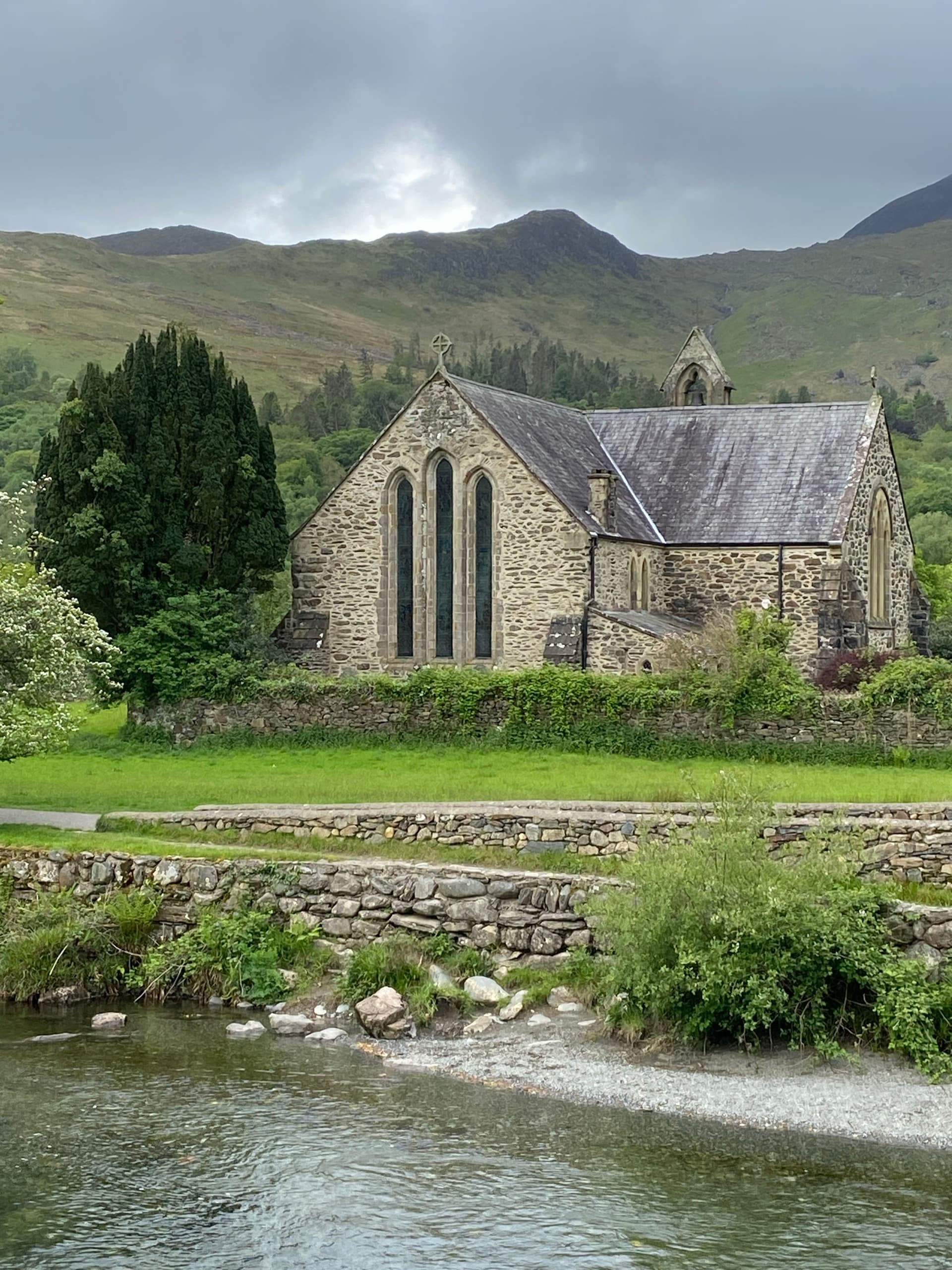 Stone church beside a river with mountains in the background