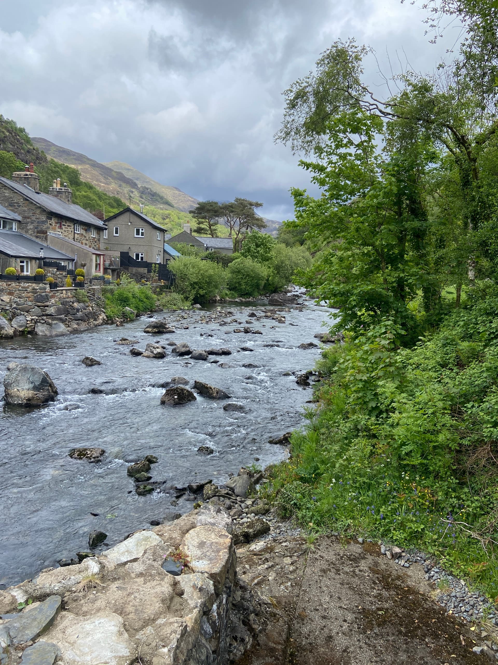 Stone cottages beside a rocky river under a cloudy sky