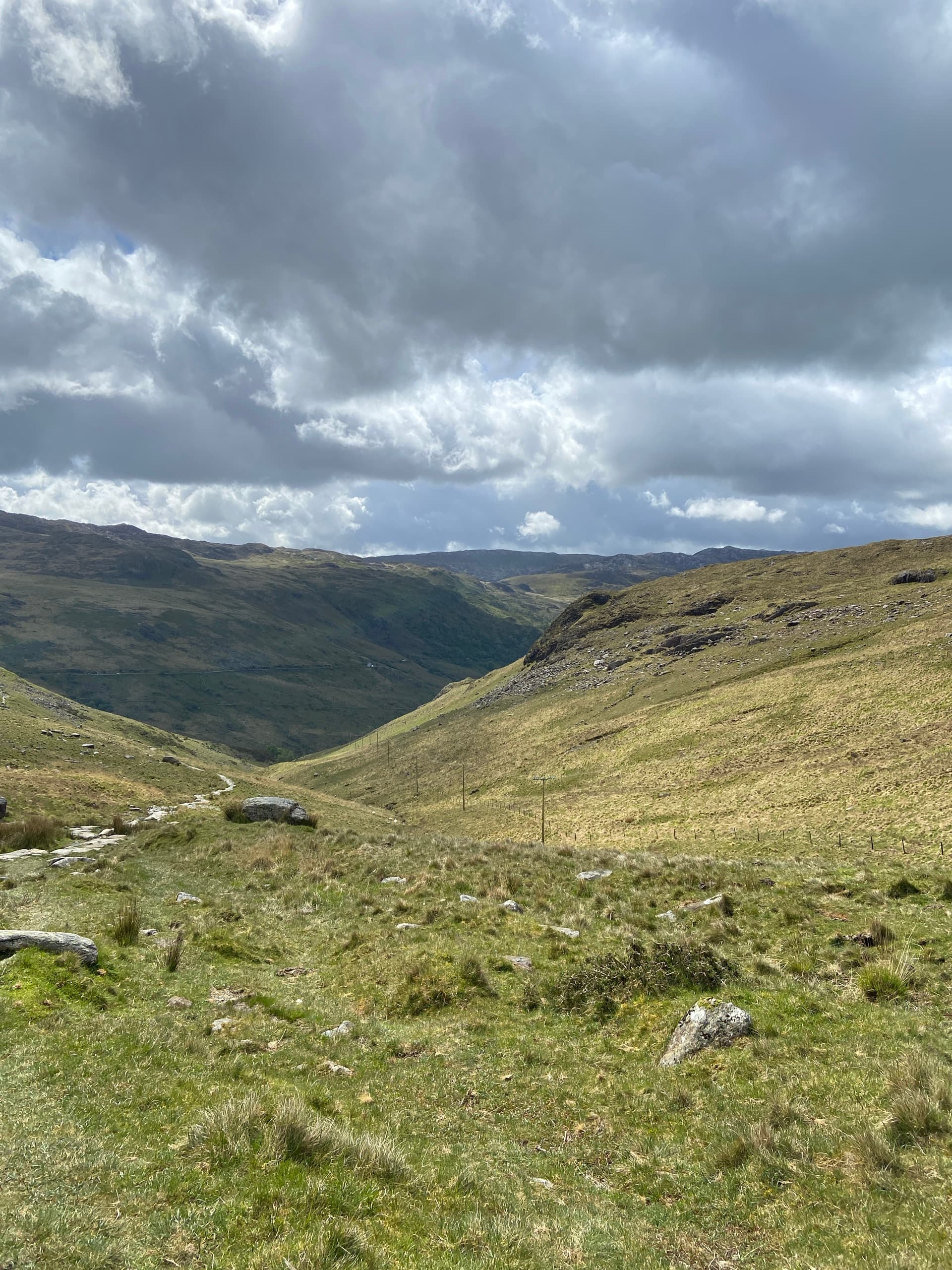 Wide grassy valley between rolling hills under dramatic stormy clouds