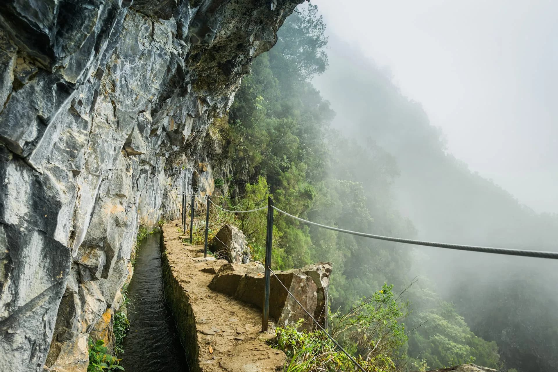 Hiking on Levada do Caldeirão path carved into a cliff face in heavy fog.