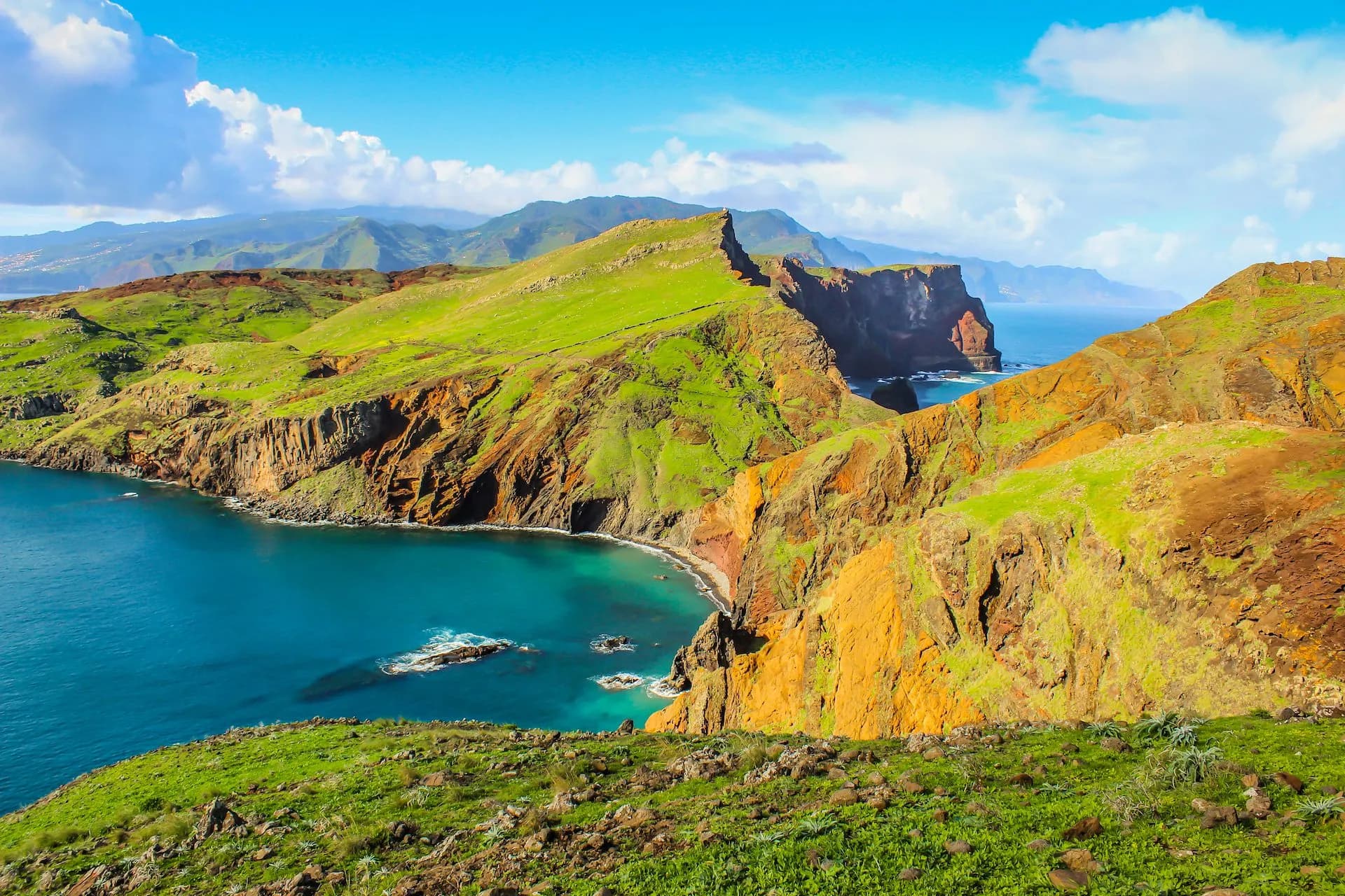Ponta de São Lourenço coastal cliffs with green hills meeting turquoise sea under blue sky.