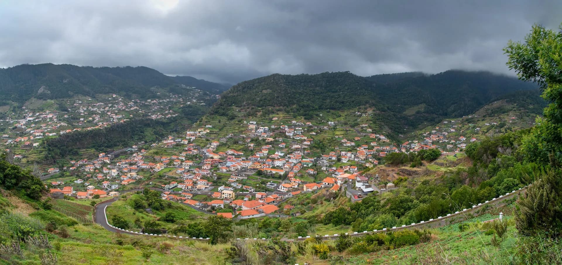 View from Levada do Caniçal showing terraced green hillsides dotted with houses under a cloudy sky.