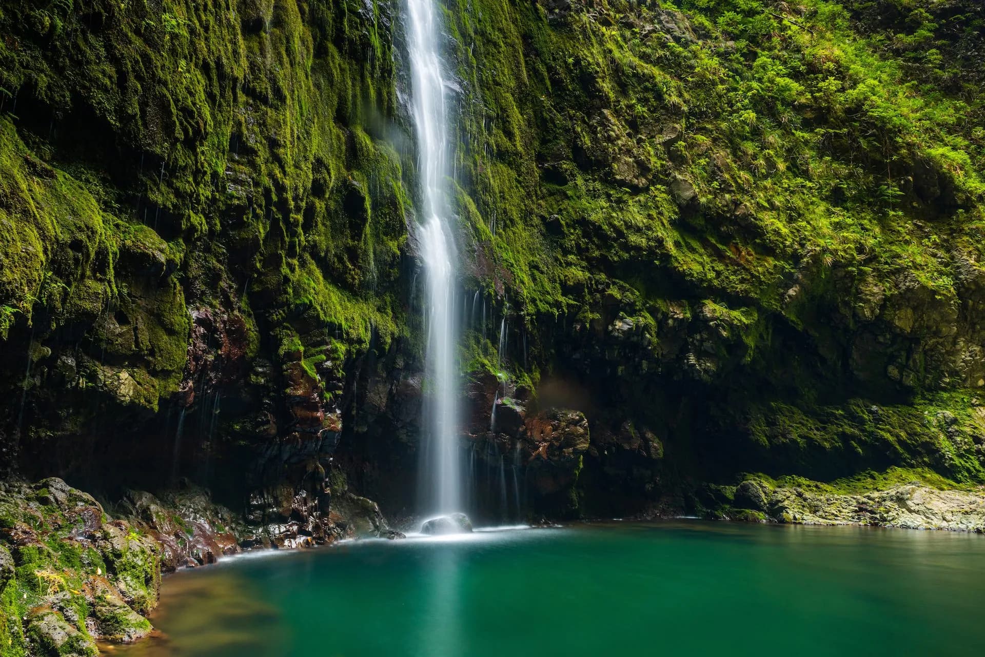 Waterfall cascading down moss-covered cliffs into a vibrant green pool at Caldeirão Verde.