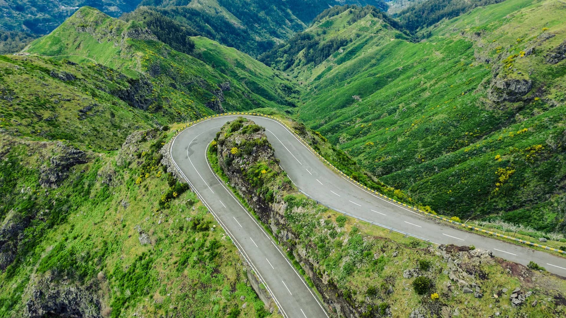 Winding mountain road descending through lush green hillsides near Encumeada Pass.