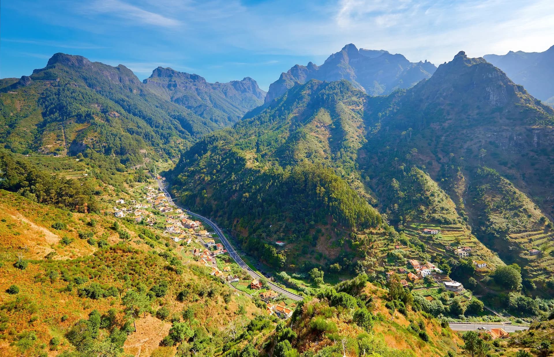 Hiking view of steep, green mountains surrounding a village nestled in a valley with a road.