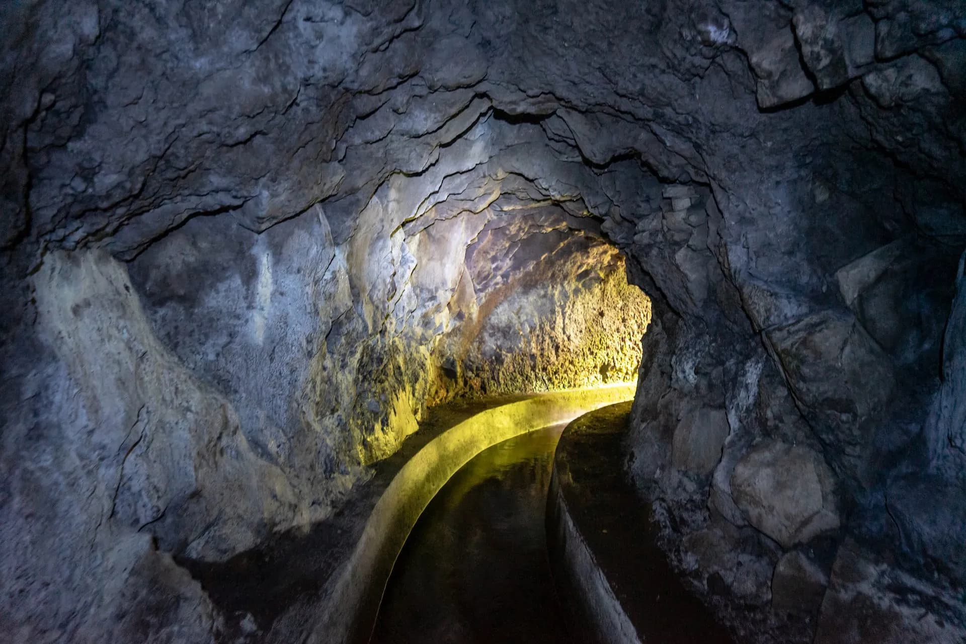 Tunnel on Levada do Norte with water channel carved through dark, rough rock walls.