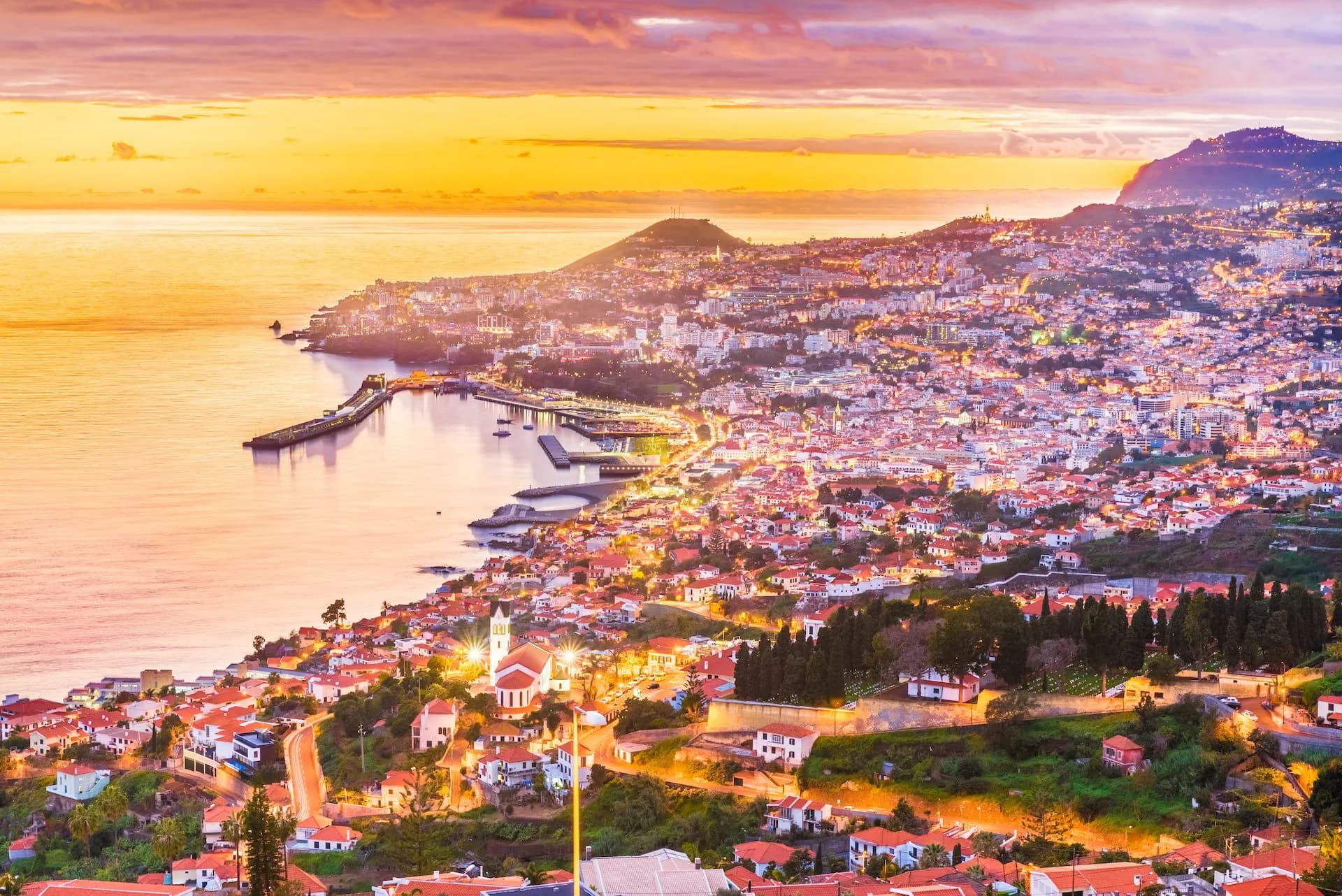 Cityscape of Funchal, Madeira, illuminated at sunset overlooking the harbor and Atlantic Ocean.