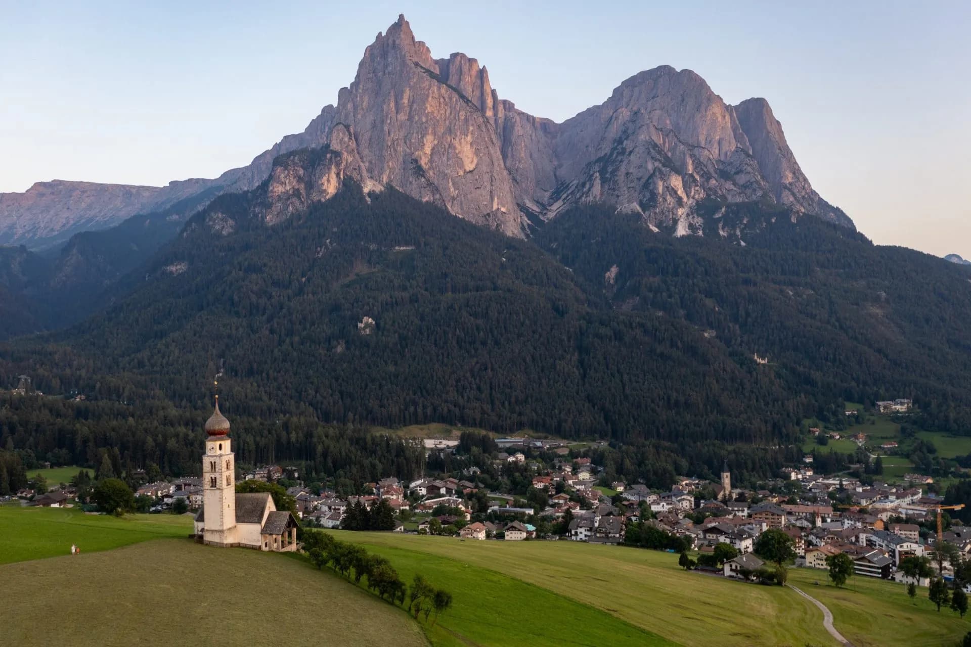 Church below massive rocky mountains overlooking a small town in a green valley.