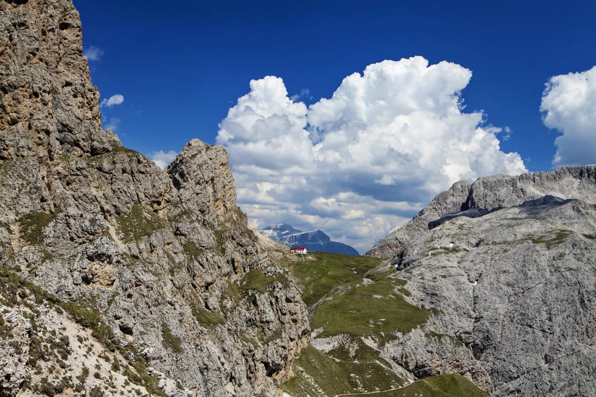 Rugged alpine mountains framing a small building with a red roof under a bright blue sky.