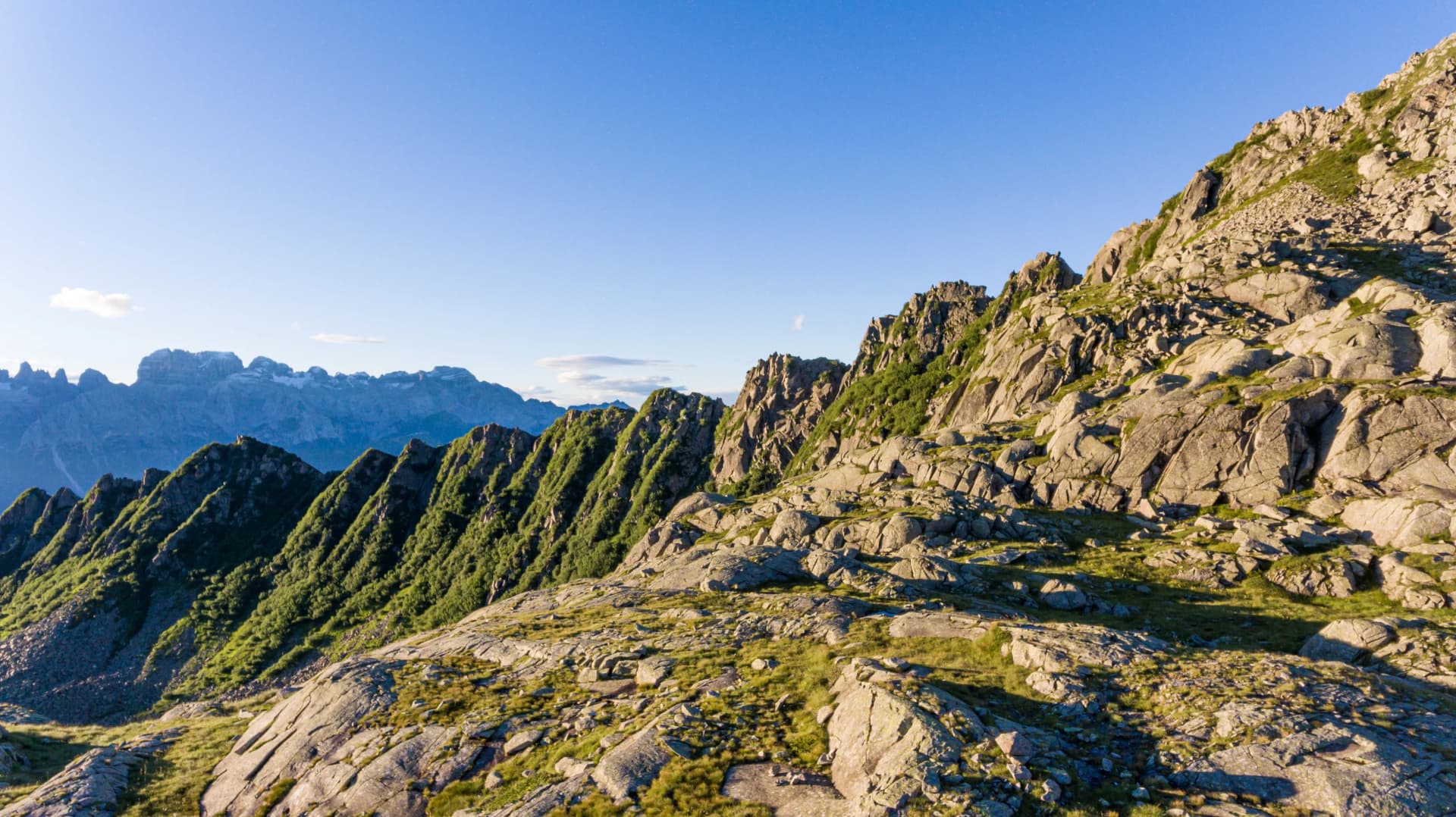 Rocky alpine landscape with green slopes and distant glacier lakes in the Italian Dolomites