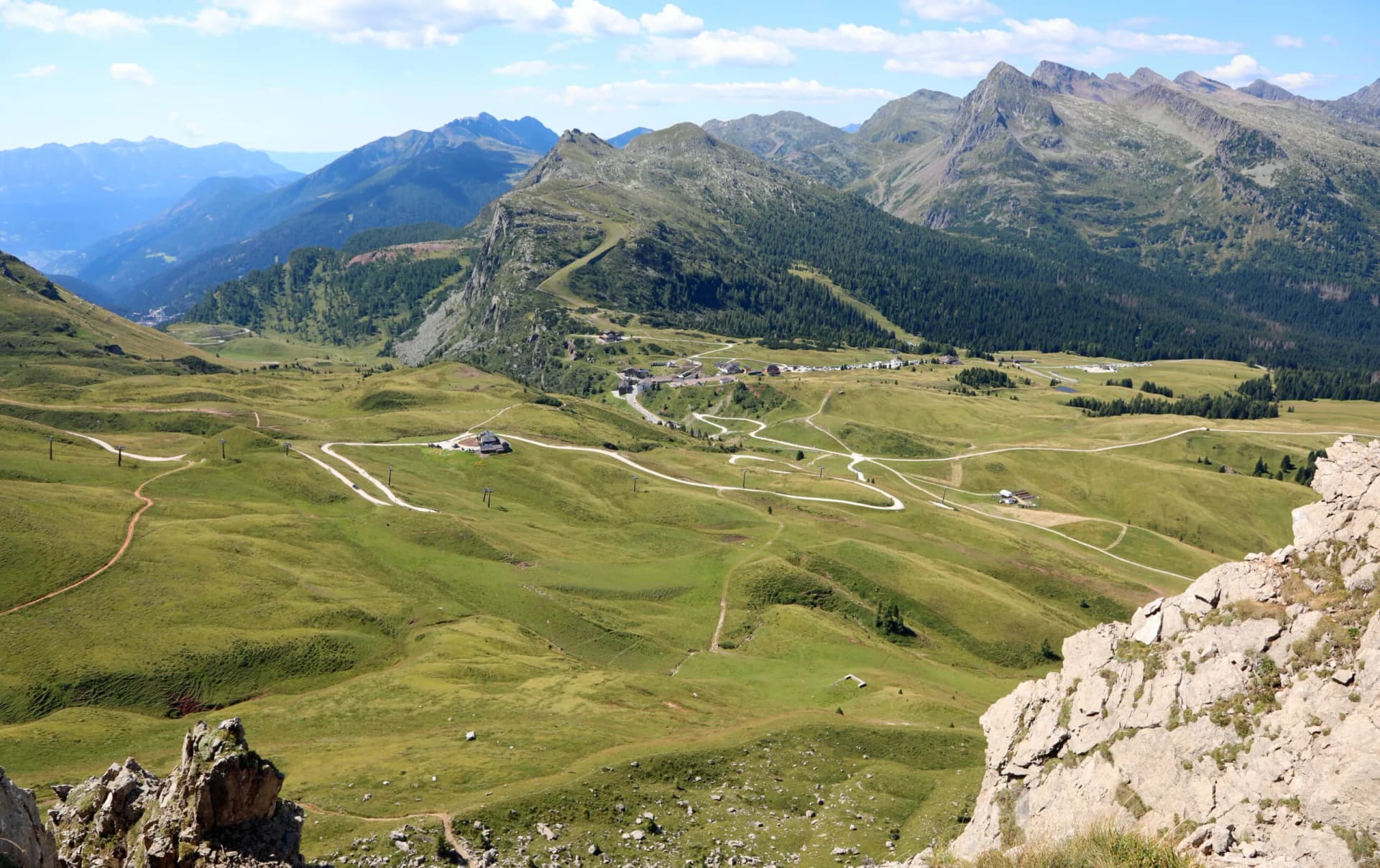 Mountain pass in Italy with green grassy meadows, winding roads, and distant peaks in summer.