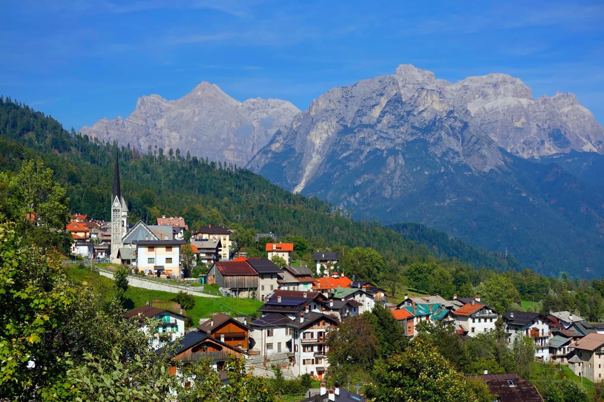 Alpine village near San Martino di Castrozza with houses nestled below jagged, gray mountain peaks.