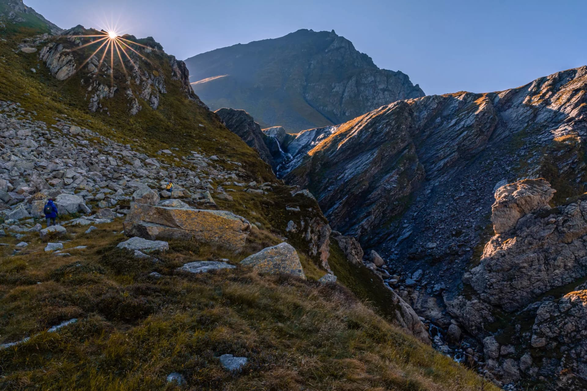 Alpine landscape near the Scaletta hut, in Blenio, Ticino, Switzerland. The sun has just risen and peeps out of a mountain in front of the observer. On the left side of the scene is a rockslide.