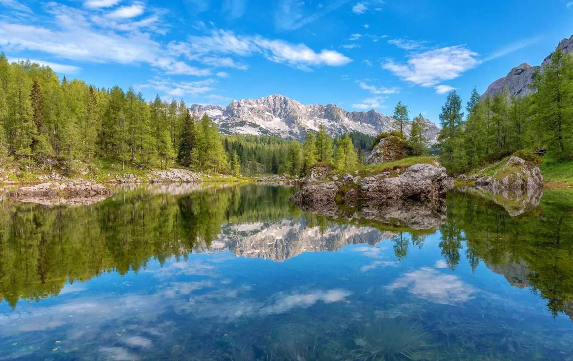 Mountain reflection in clear lake surrounded by green forest under blue sky, Valley of the Seven Lakes.