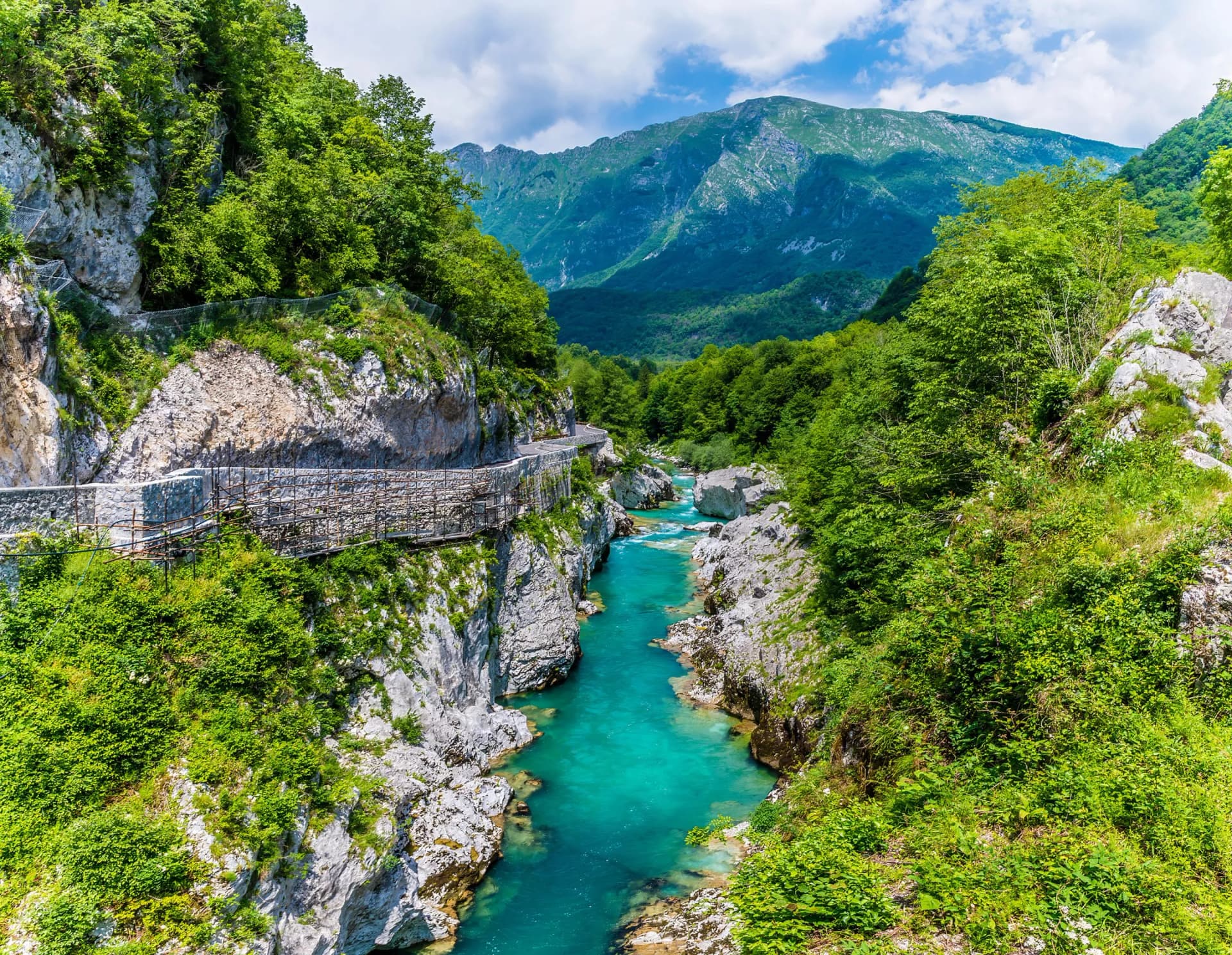 View up the Soca River from Napoleon Bridge in Slovenia, showing turquoise water and lush mountains in summertime.