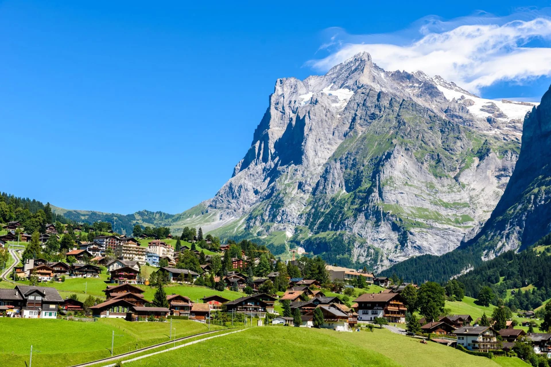 Alpine village of Grindelwald nestled in green valley below massive, snow-capped Eiger mountain.